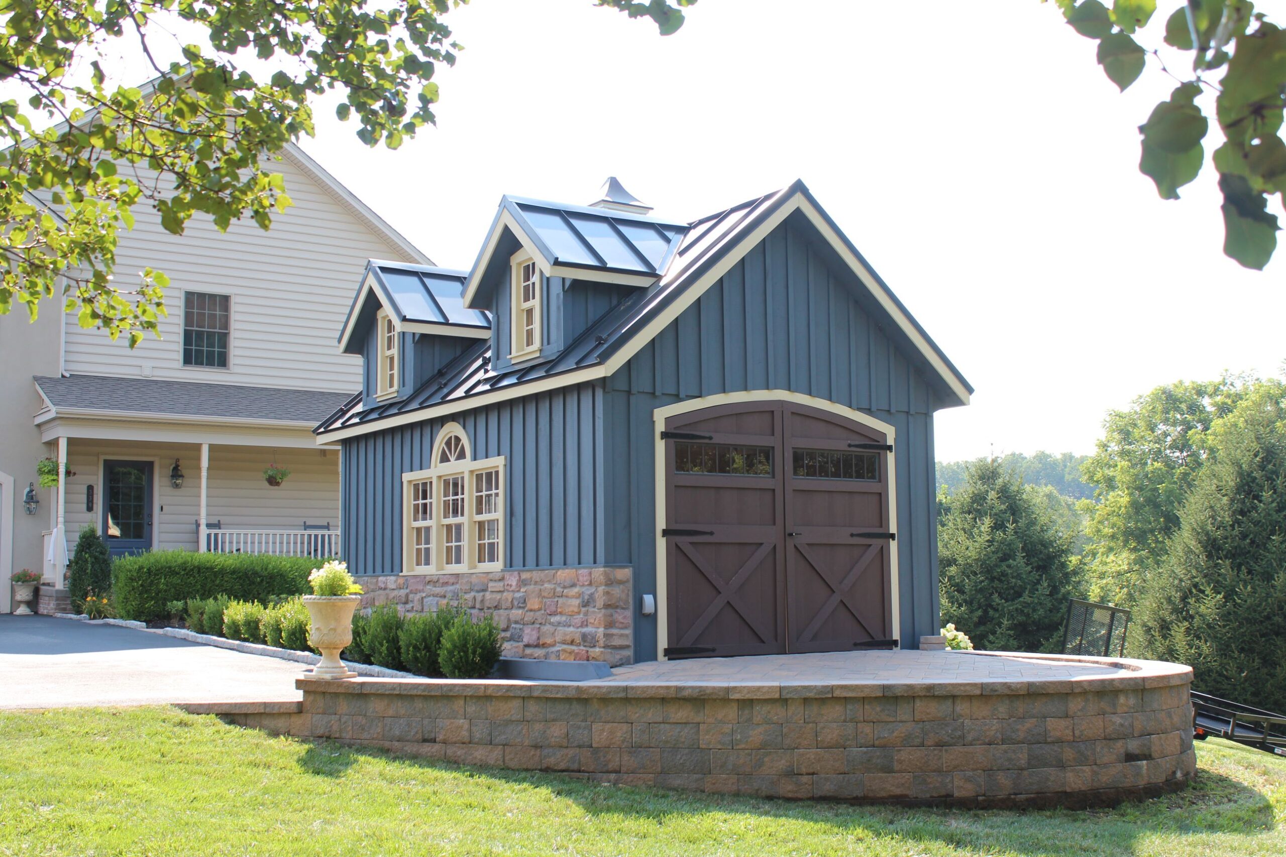 Front and side exterior of a New England Barn Shed with blue siding, stone accents, and white trim.