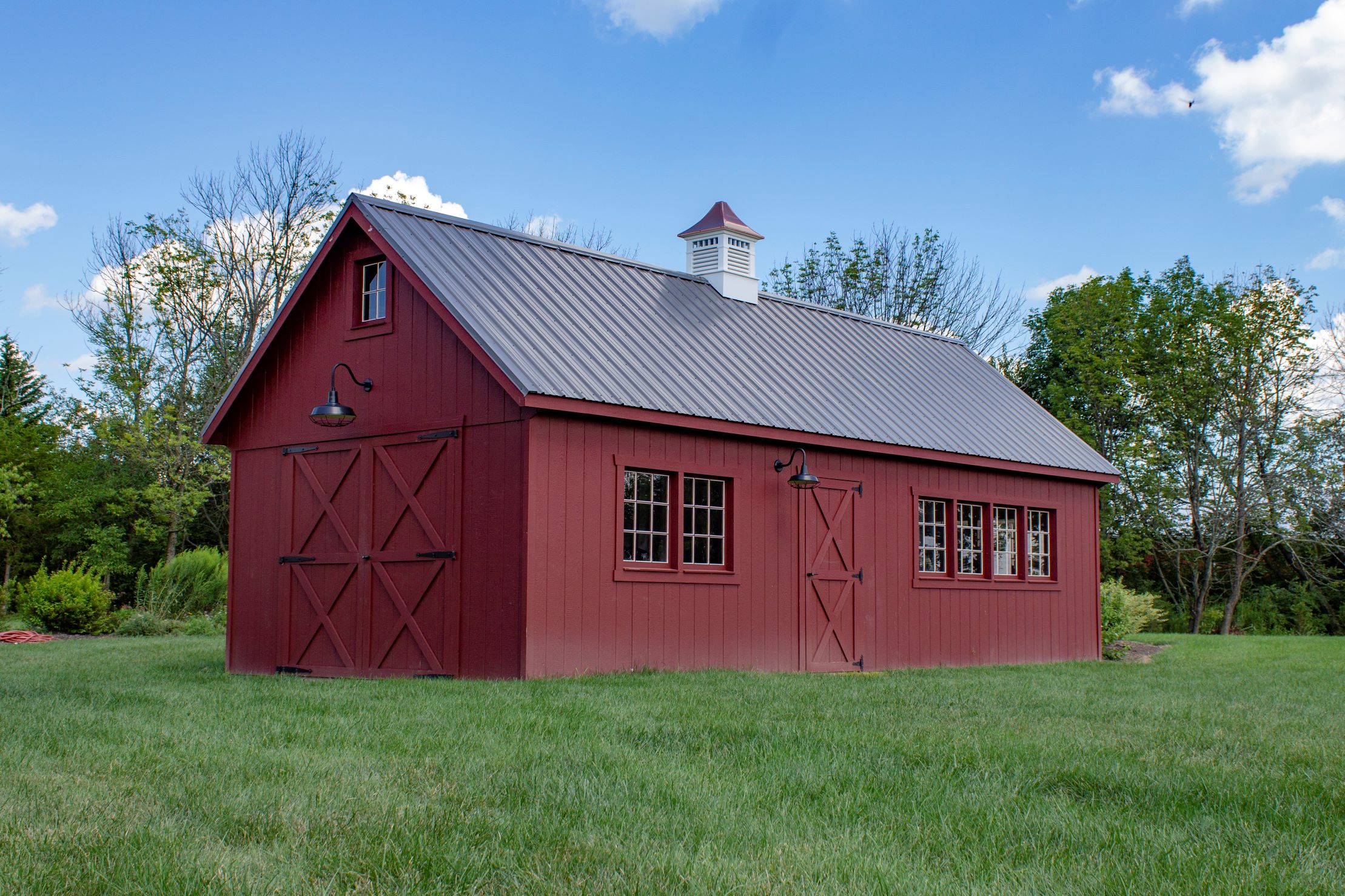 Front and side exterior of a large New England Barn Shed with red siding and light gray roofing.