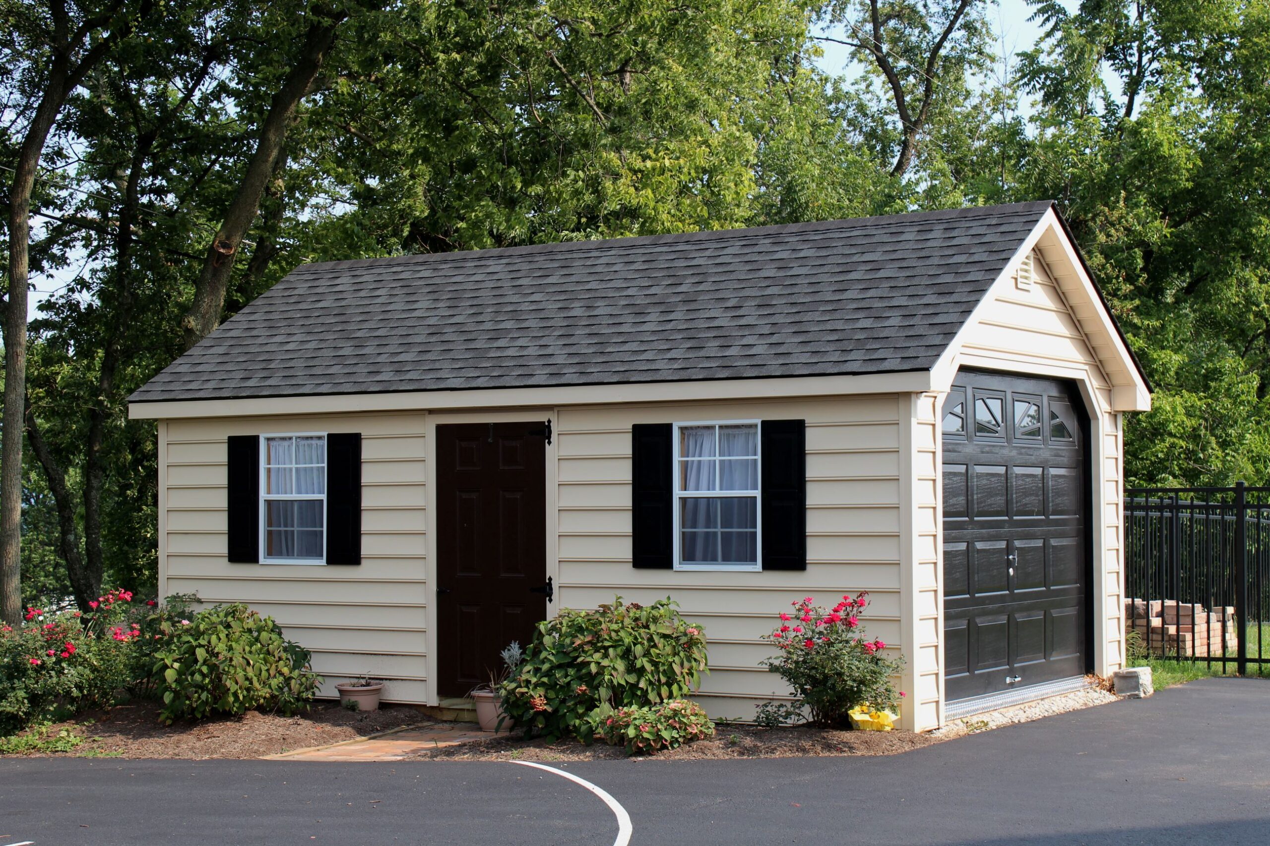 Exterior of a 1-story, 1-car Garden Shed Garage with beige siding and black doors.