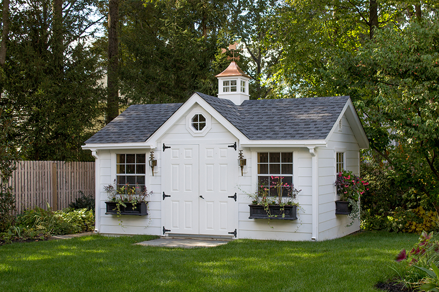 Front exterior of a Victorian Shed with white siding, gray siding, black flower boxes, and a copper cupola.