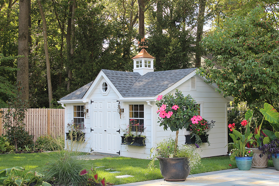 Front and side exterior of a Victorian Shed with white siding, gray siding, black flower boxes, and a copper cupola.
