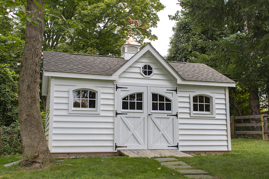 Front exterior of a Victorian Shed with white siding, brown roofing, and a copper cupola.
