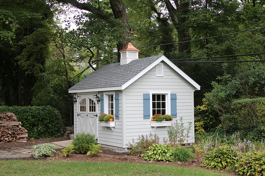Front and side exterior of a Garden Shed with light gray siding and blue shutters