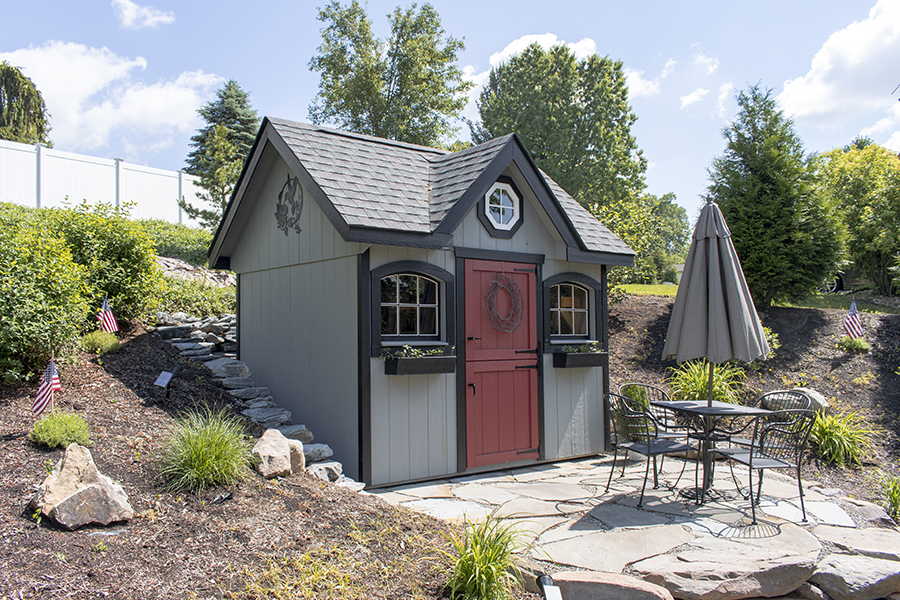 Small Victorian Shed with gray siding, black trim, and a red door.