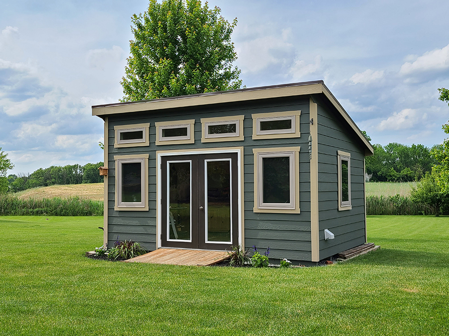 Front exterior of a Studio Shed with green siding and beige trim.