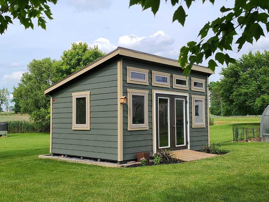 Front and side exterior of a Studio Shed with green siding and beige trim.