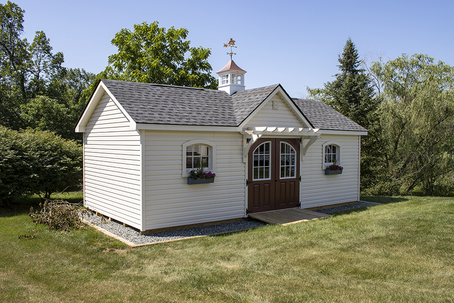 Front and side exterior of a Victorian Shed with white siding, gray roofing, brown double doors, and a copper cupola.