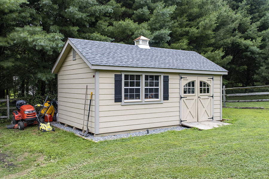 Front exterior of a Garden Shed with tan siding, black shutters, and a gray roof.