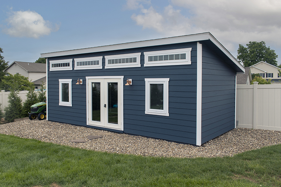 Front and side exterior of a Studio Shed with blue siding and white trim.
