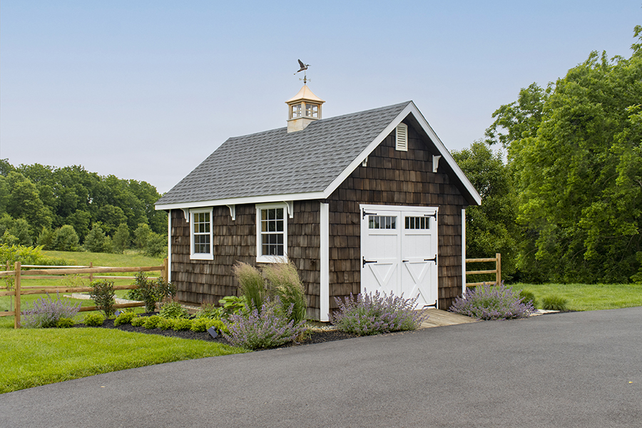 Colonial Garden Shed with brown wood siding, white trim, white double doors with windows, and a gray roof with a cupola.