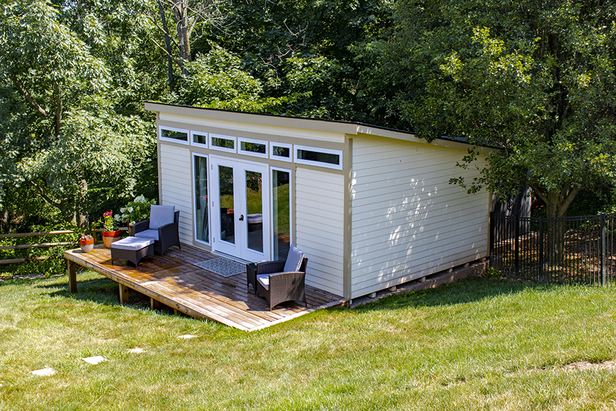 Front and side exterior of a Studio Shed with white siding and tan trim.