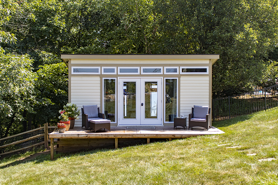 Front exterior of a Studio Shed with white siding and tan trim.