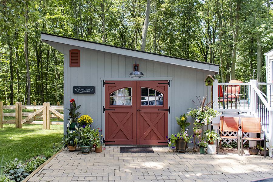 Front exterior of a Studio Shed with light gray siding and red double doors.