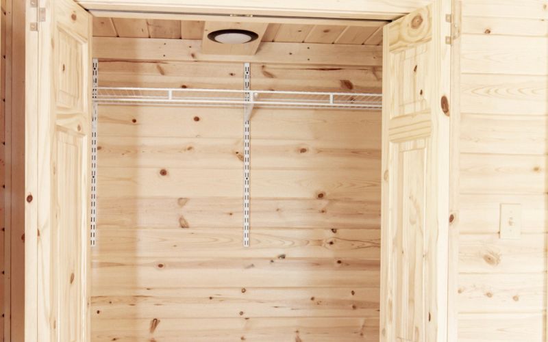 Close up of the inside of a pine closet in a cabin with shelving and a light
