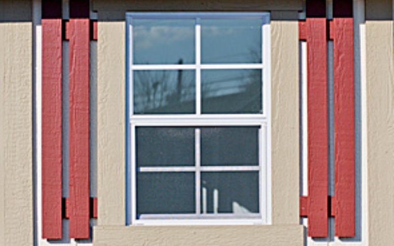 Close up of a tan and white window with red slat shutters