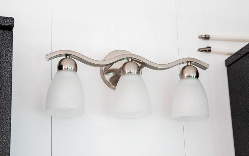 Close up of a wall-mounted white and silver triple vanity light