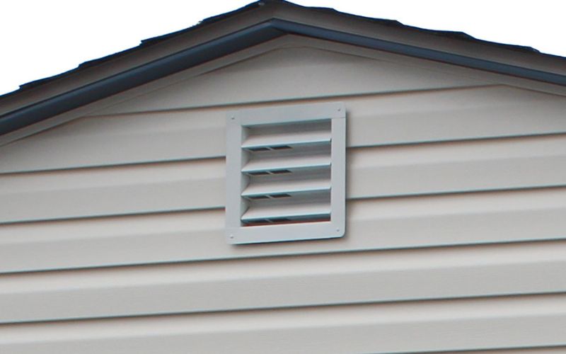 Close up of a white basic metal gable vent on a beige vinyl shed