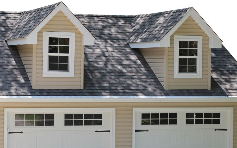 Close up of a cape cod dormer on a garage with yellow siding, white trim, and dark gray roofing
