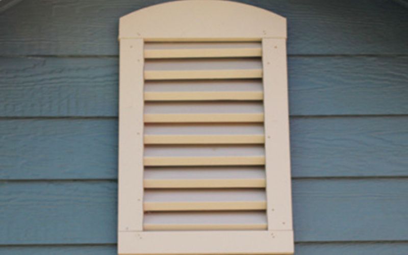 Close up of a beige decorative gable vent on a blue building