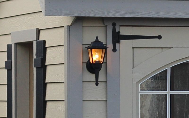 Close up of a black exterior light sconce installed on a gray and tan building