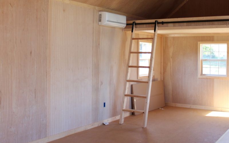 Interior of a shed with beaded plywood walls and a loft with a ladder