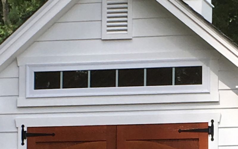 Close up of a shed's long Vinyl Insulated Transom Window in white above a red door