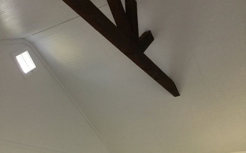 Close up of a shed ceiling with a white painted interior and wood beam decor