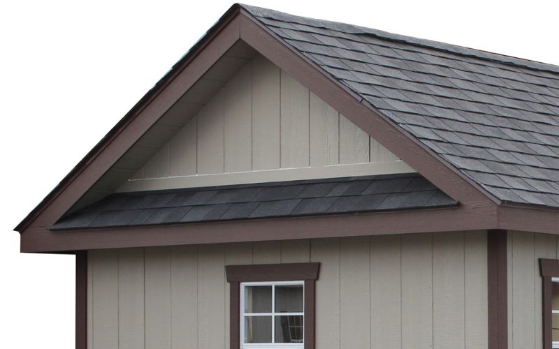 Close up of a pent roof overhang with light gray siding, brown trim, and dark gray roofing