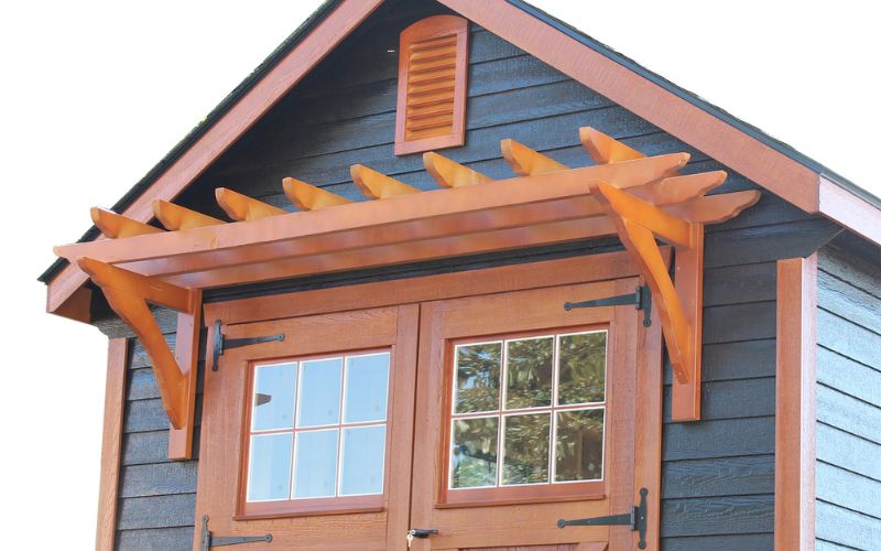 Close up of a brown pergola overhang on a shed with black siding and brown trim