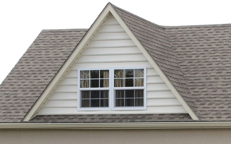 Close up of a reverse gable on a building with white siding, white trim, and and light brown roofing