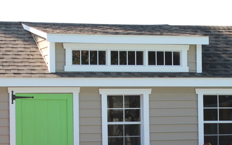 Close up of a transom dormer on a shed with gray siding and white trim