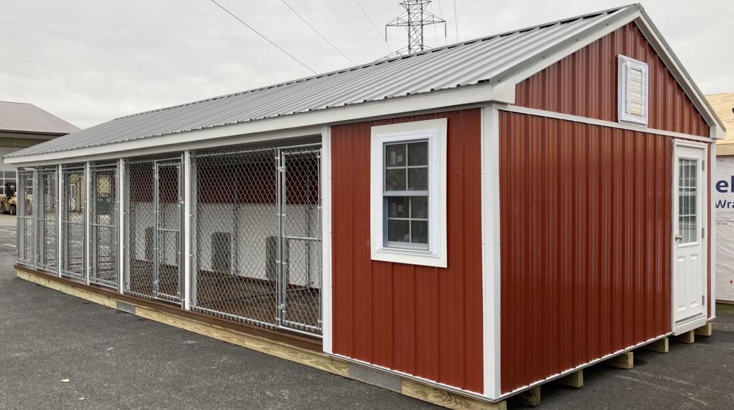 Front and side exterior view of a 14x36 commercial kennel with red siding, white trim, gray metal roofing, a white window, a white entry door, and 6 dog runs.