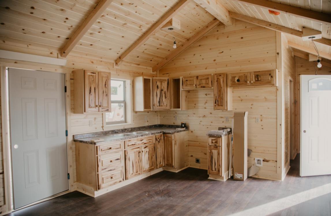 Interior of a custom 14x50 log cabin's kitchen with natural wood walls and cabinets.