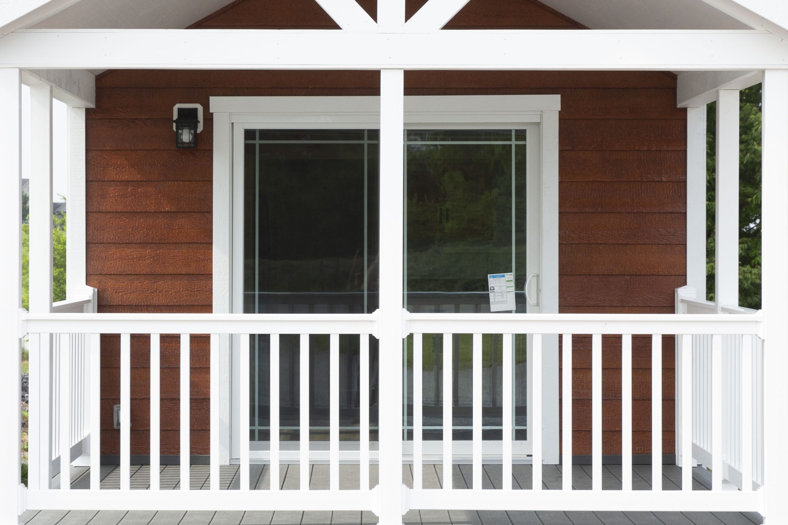 Close up of an Appalachian Park Model's entrance with brown wood siding, white trim, glass double doors, and a white fenced-in porch.