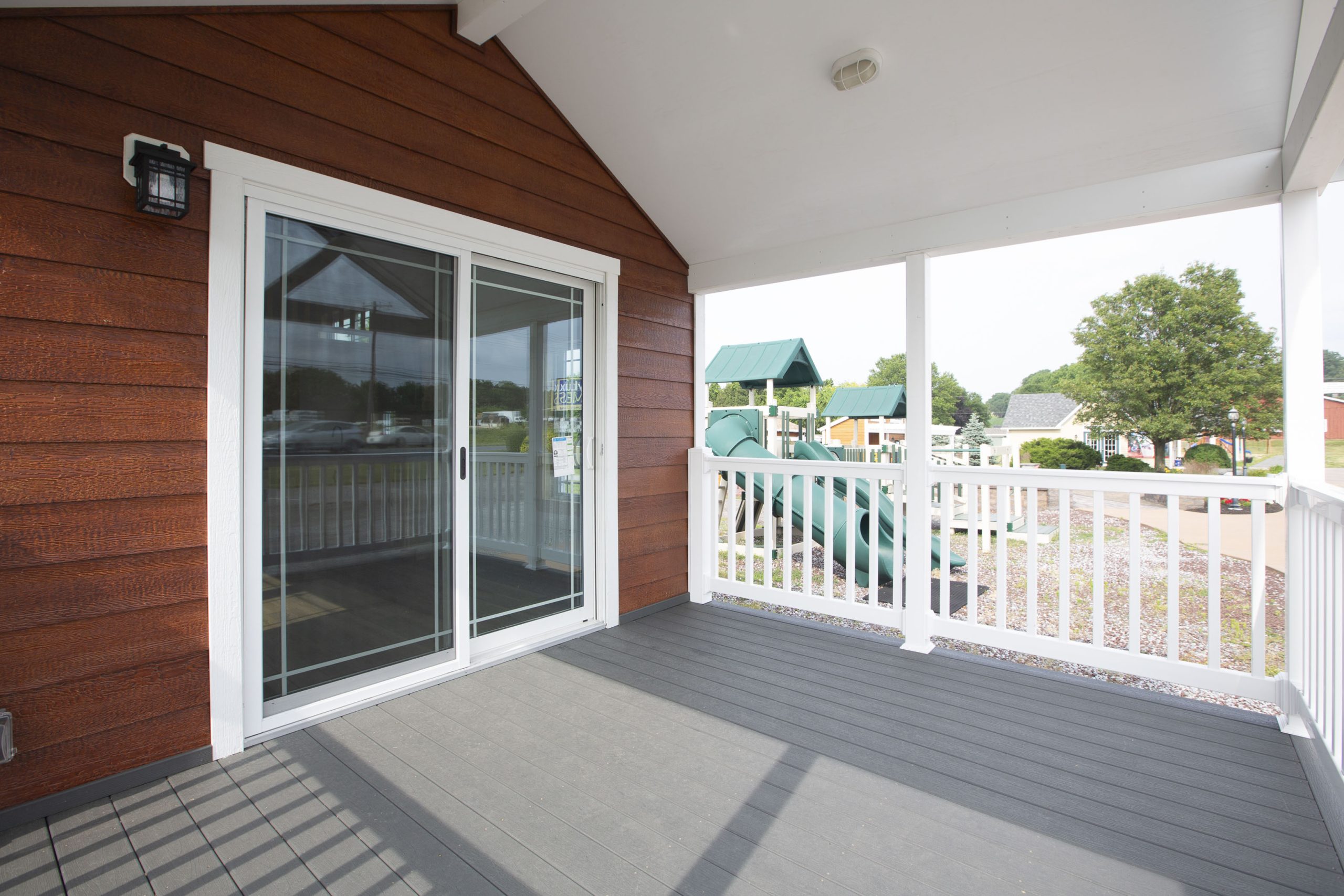 White fenced-in porch on an Appalachian Park Model with brown wood siding, white trim, and glass double doors.