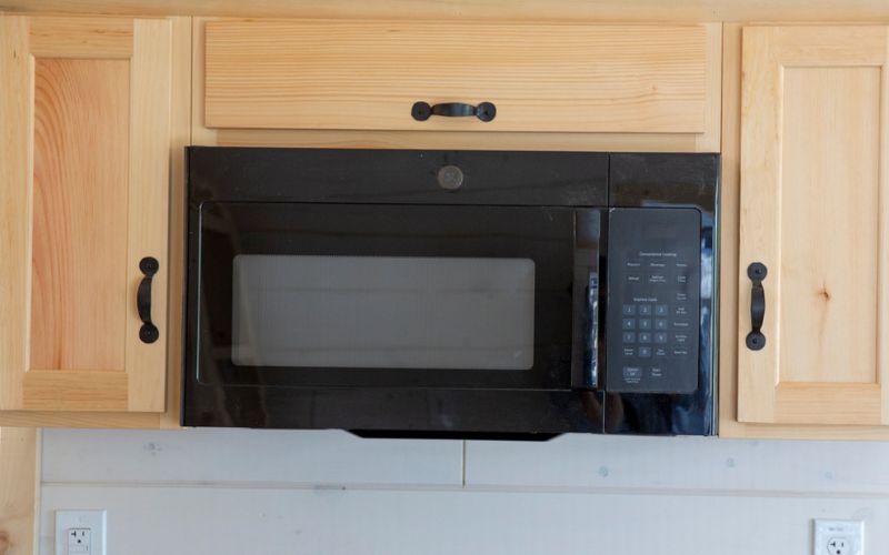 Black microwave with natural wood cabinets built around it.