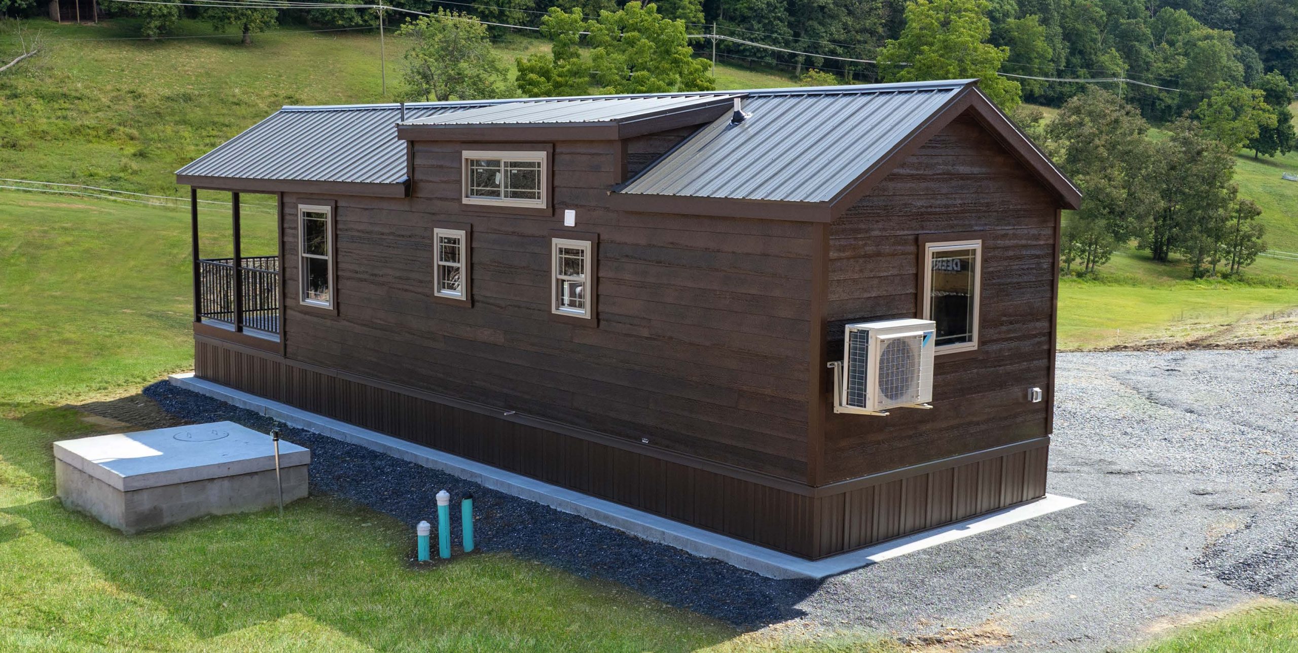 Back exterior of a Pine Cone Park Model with stained wood siding, brown trim, a brown metal roof, and white windows.