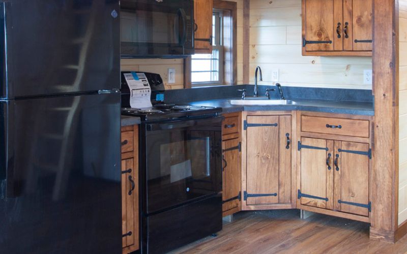 Kitchen with dark laminate countertops, rustic wood cabinets, a black fridge, a black microwave, and a black oven with a range coil stove.