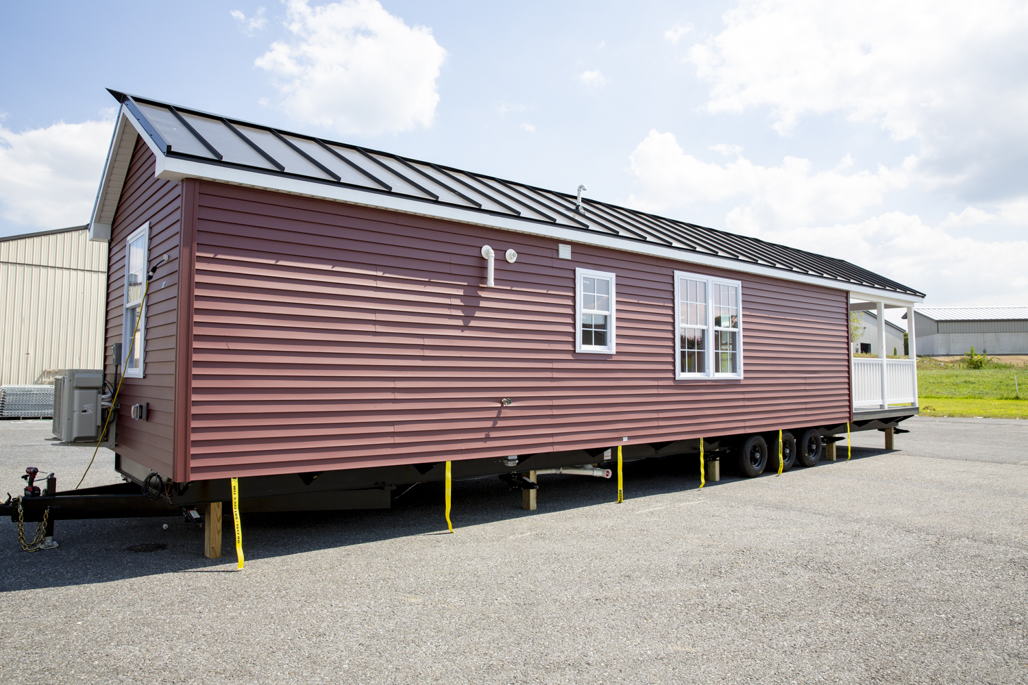 Back and side view of a Santa Rosa Park Model with red vinyl siding, white windows, white trim, a white fenced-in porch, and a dark metal roof.