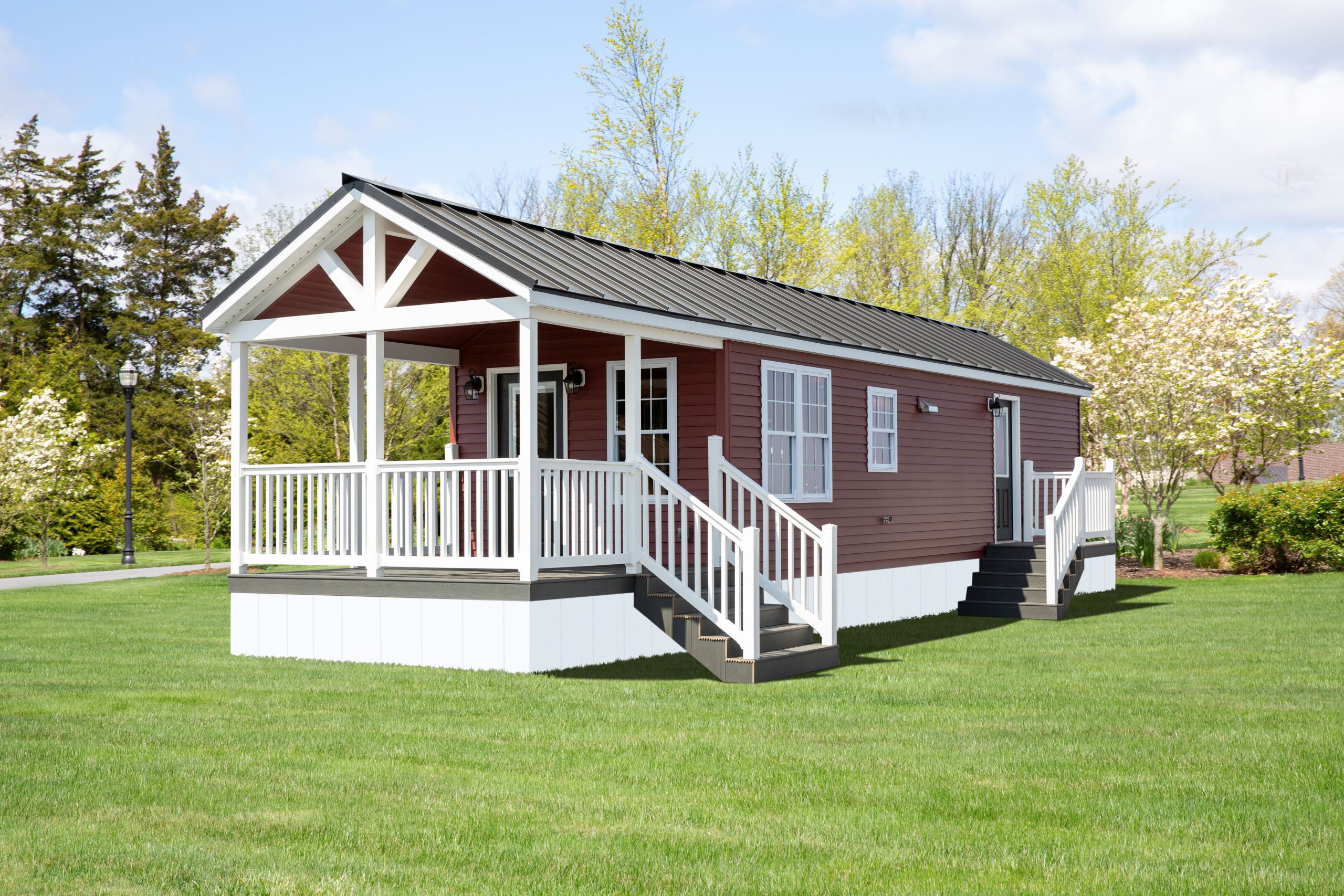 Front and side view of a Santa Rosa Park Model with red vinyl siding, white windows, white trim, a white fenced-in porch, a side entrance with steps, and a dark metal roof.