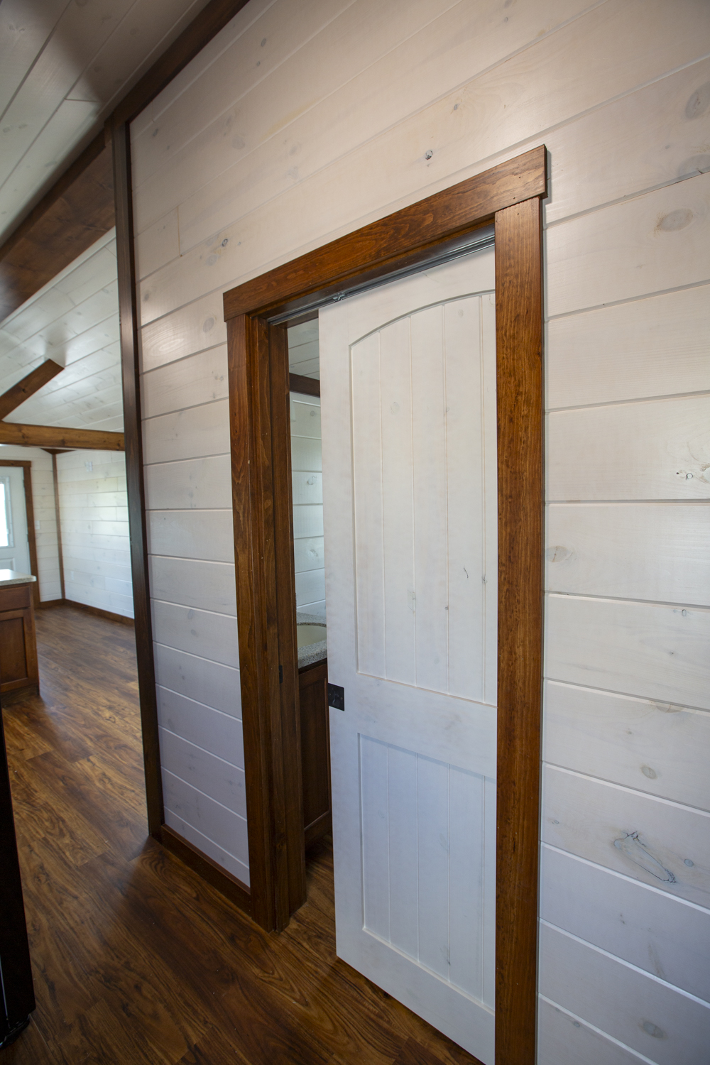 Hallway interior of a Santa Rosa Park Model with white wood plank woods, brown wood trim, vinyl plank flooring, and a white pocket door.