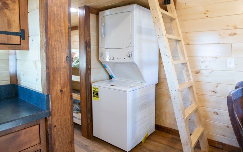 White stacked washer and dryer in a corner under a loft ladder.