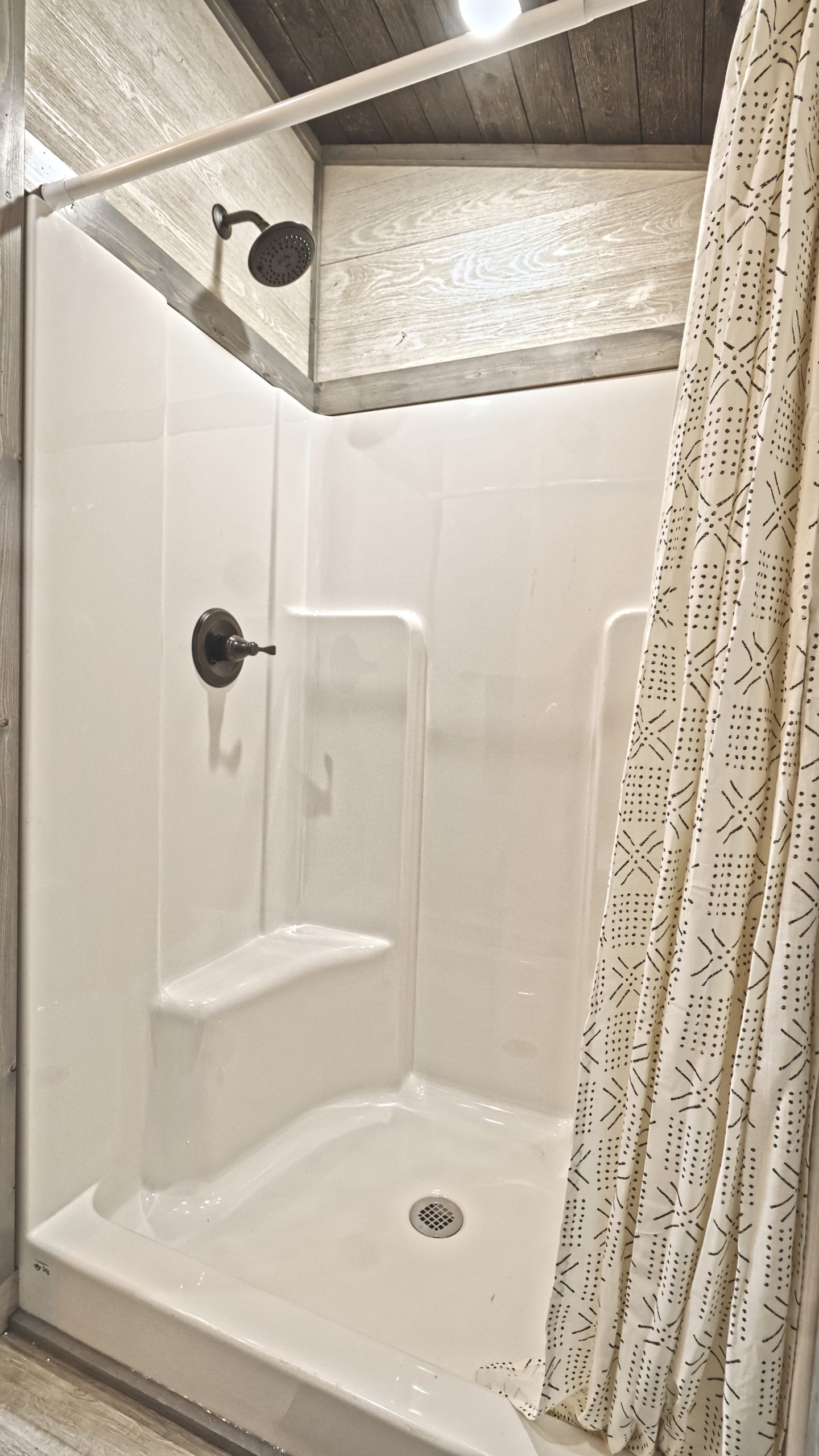 Close up of a standing shower in a Meadowlark Park Model bathroom with white walls and a white patterned shower curtain.