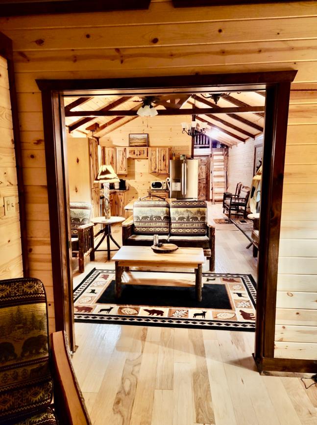 Interior of a decorated 16x60 custom cabin with a natural wood coffee table, a bear themed loveseat, and an assortment of rustic decor.