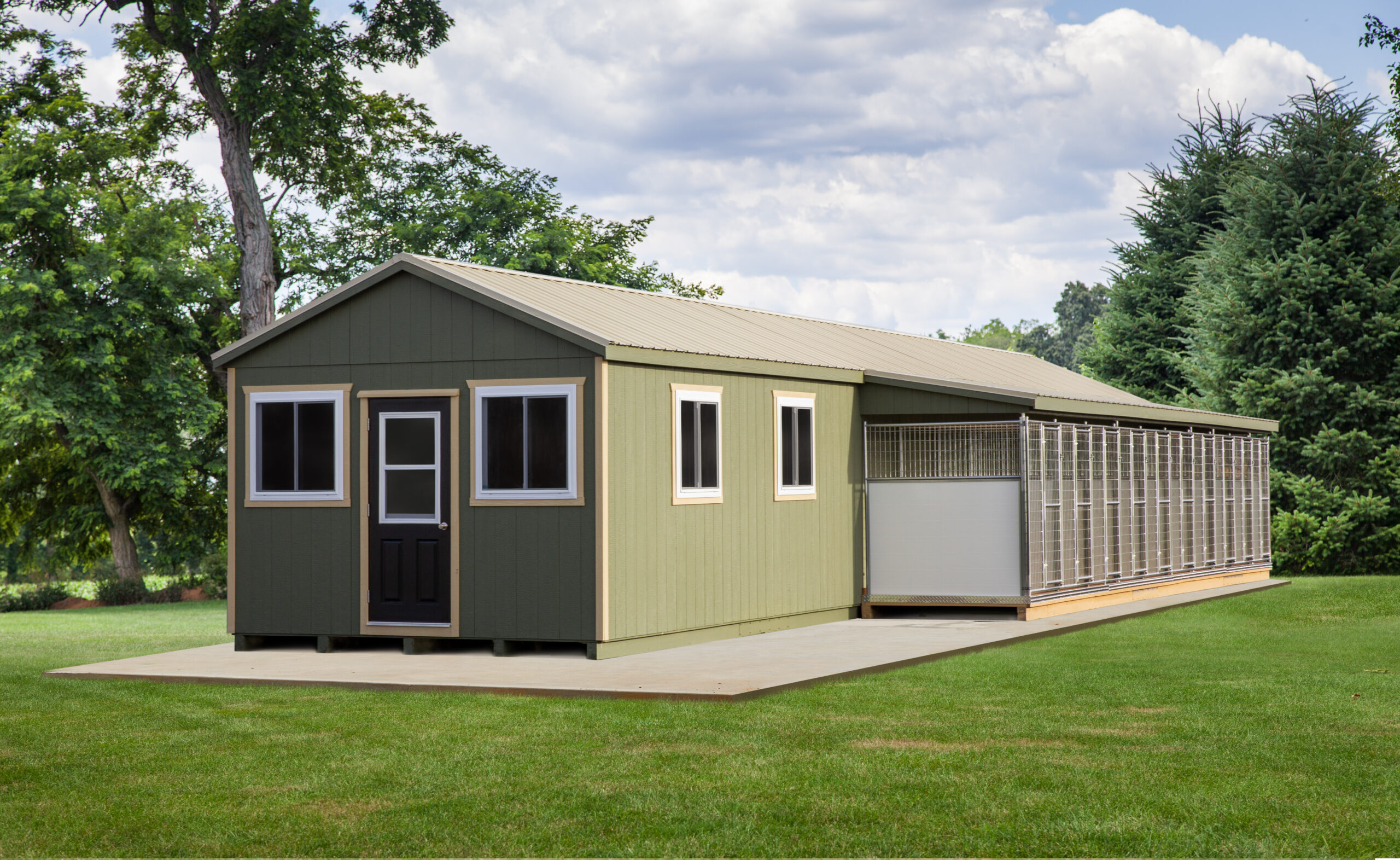 Back and side view of a commercial dog kennel with green siding, tan trim, 4 white windows, and a row of dog runs.